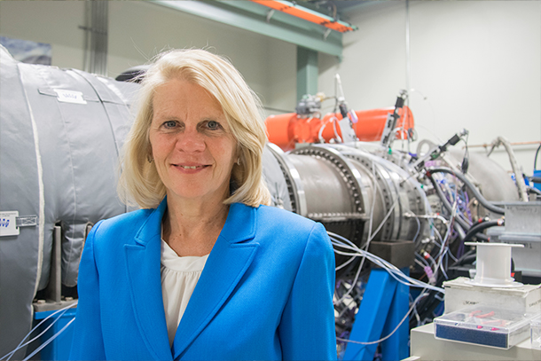 An indoor portrait of an individual standing in front of a gas turbine. 