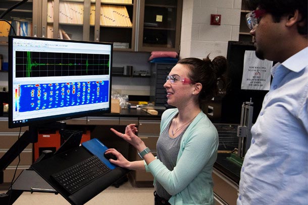 Two researchers examine an ultasonic wave readout on a computer monitor.