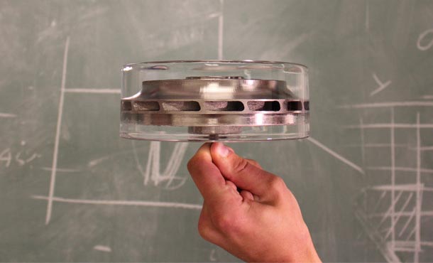 A hand holds a cylindrical metal part almost entirely encased in a cylindrical block of crystal-clear ice