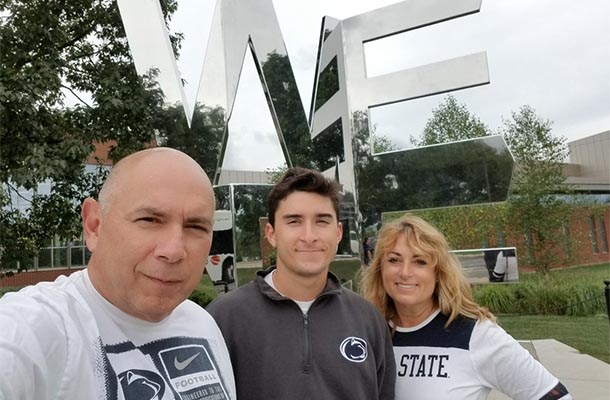 Three people pose in front of the We Are statue on Penn State campus