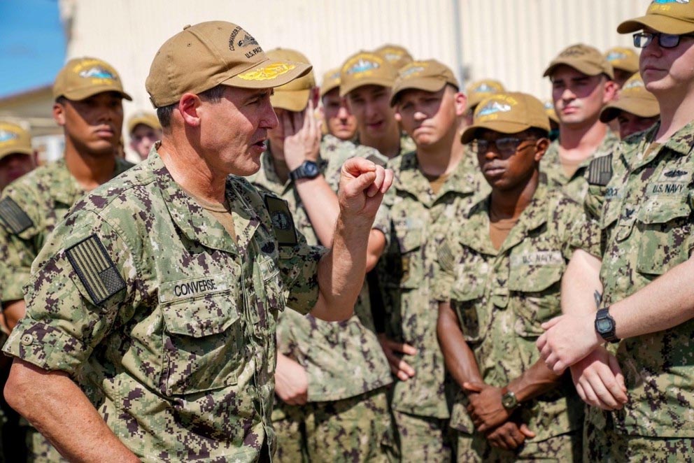 A naval officer addresses sailors, all dressed in camouflage.