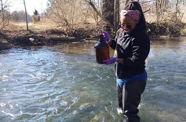 a woman wearing hip waders stands in a stream collecting water samples