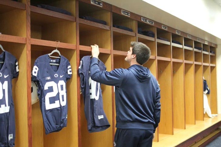 A man hangs football jerseys in the locker room.