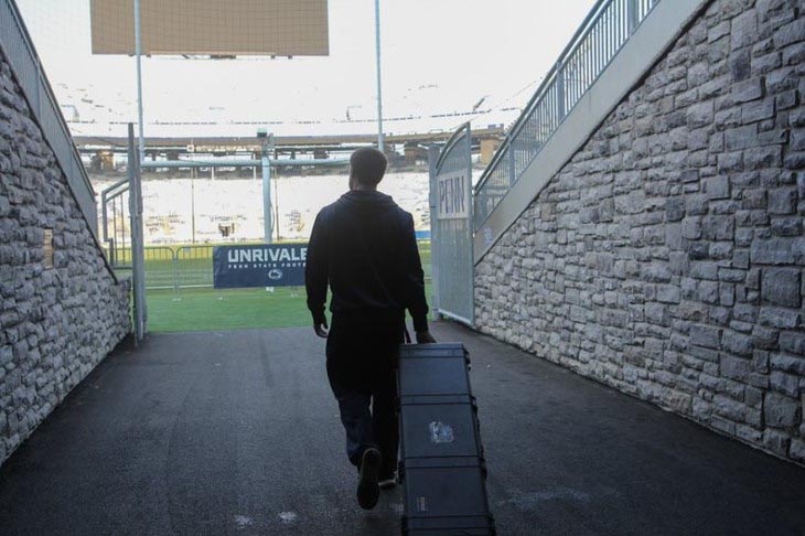 A man rolls equipment case behind him enters a football stadium.
