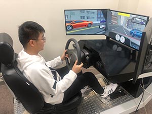 a man sits at test driving station with a steering wheel and computer screens to simulate driving on the road.