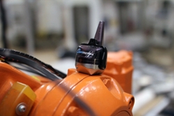 A small, black sensor sits on top of an orange machine.