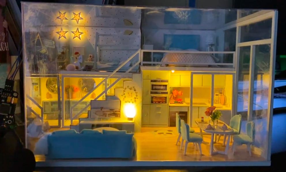 A small-scale house that fits on a table top and is outfitted with lights and small pieces of furniture, simulating a life-size smart house.