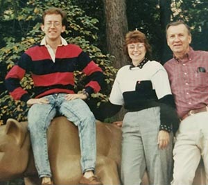 a man sits on the Penn State lion statue with his parents standing beside him.