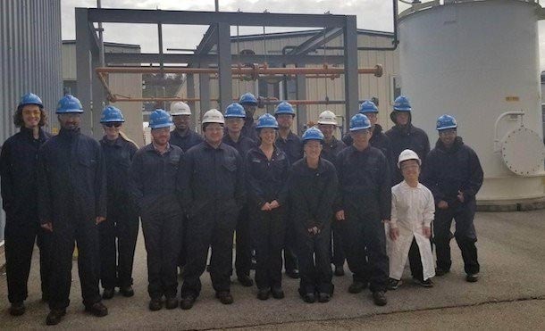 a group of people in blue coveralls inside of a chemical plant