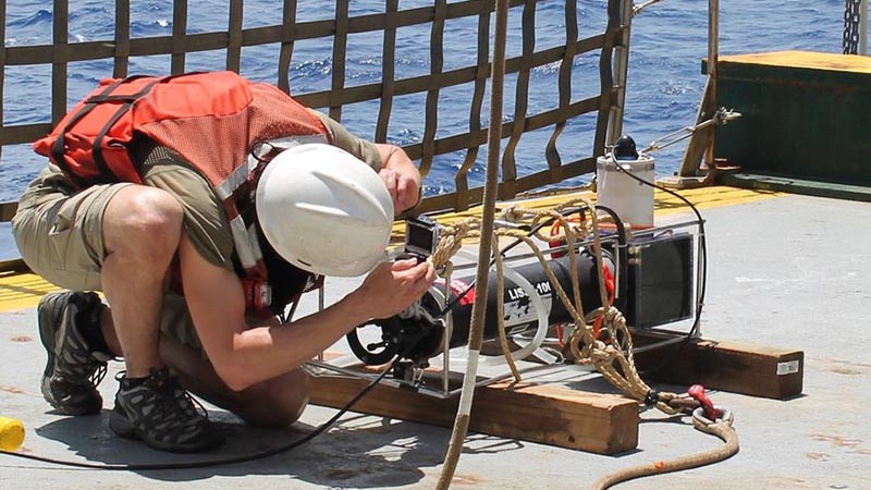 A professor leans over to examine instrumentation on a scientific ocean expedition.