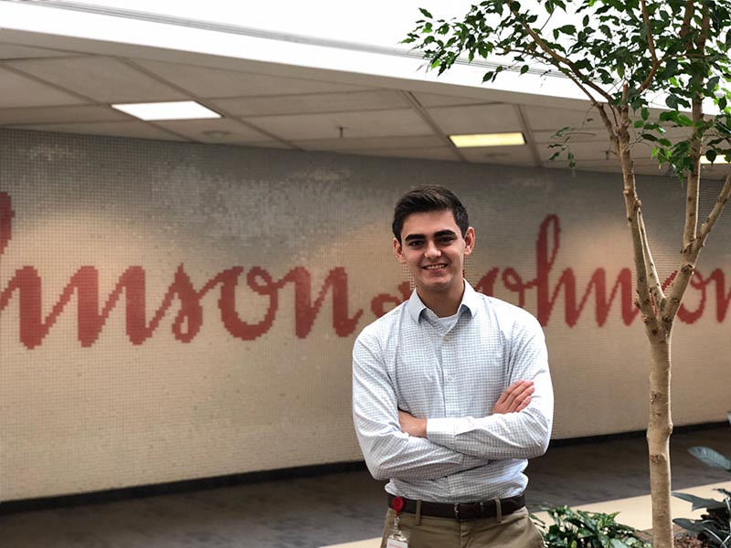 a man stands in front of a wall that displays the Johnson and Johnson logo.