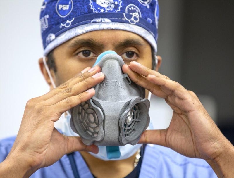 A man holds a 3D-printed filtration mask prototype to his face.