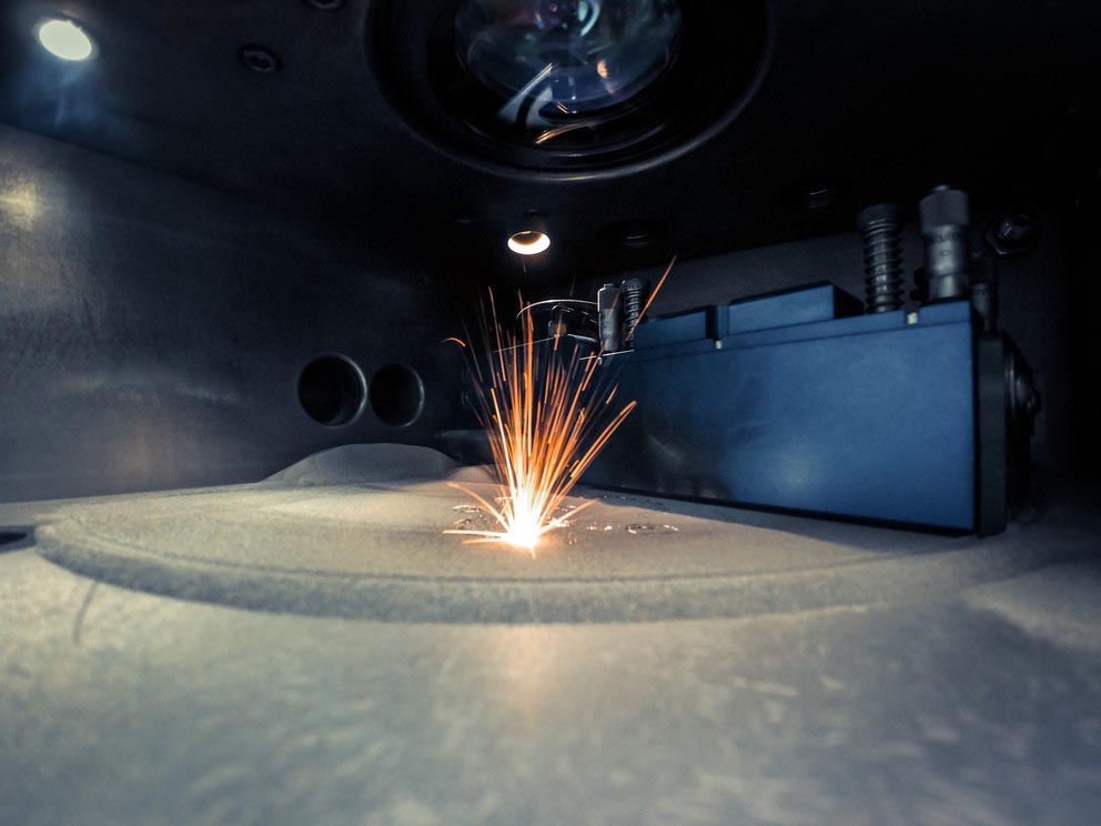 A machine 3D prints a metal objects while emitting sparks.
