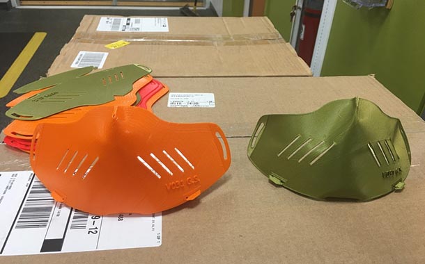 Two shaped mask shields and a stack of flat mask shields on top of cardboard boxes