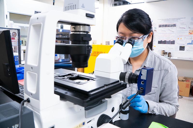 A graduate student wearing a face mask looks through a microscope.