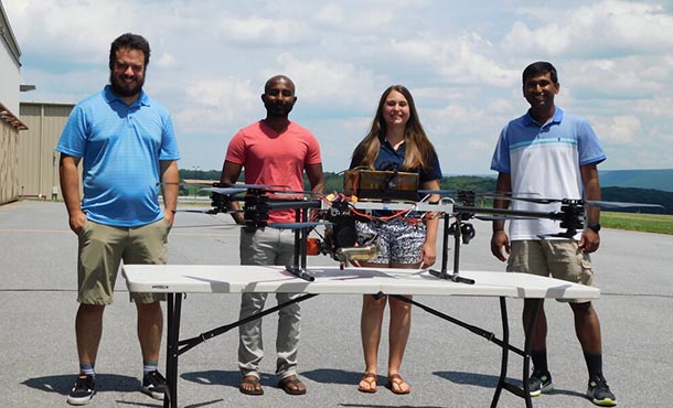 Four people stand behind a table with a large drone on top of it