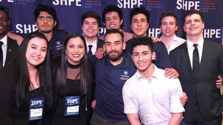 A group of students in the Penn State Society of Hispanic Professional Engineers pose in front of a branded backdrop