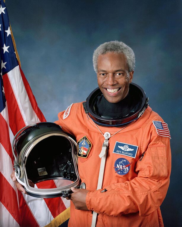 Guion Bluford posing in astronaut suit in front of American Flag