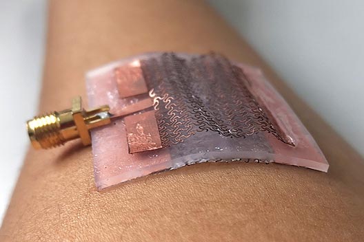 close-up of a multilayered patch being worn on a person's forearm, with the top copper mesh layer contracting upward into two arches