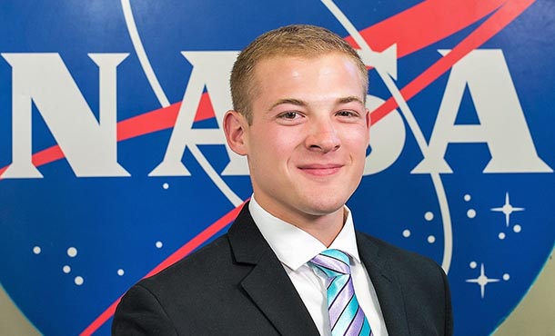 male student in business attire smiles and poses in front of the NASA logo