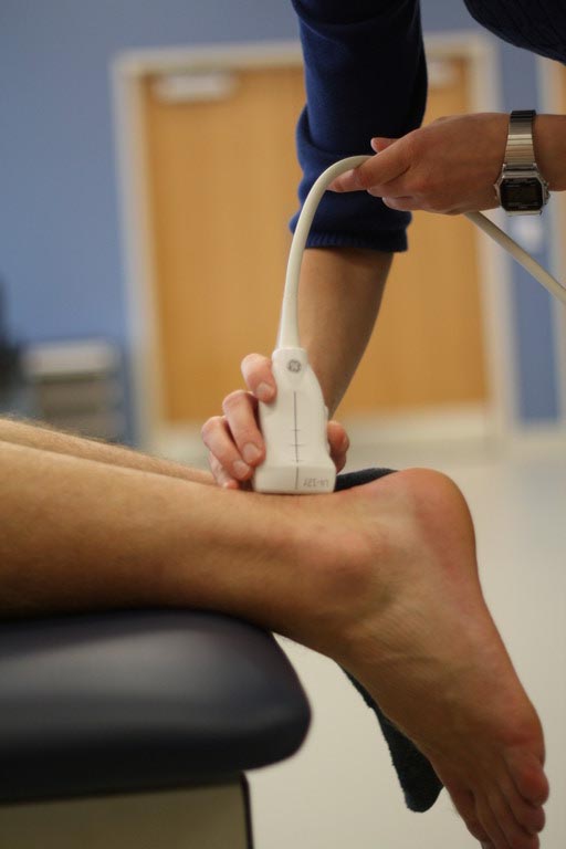 a physical therapist holds a device against the back of a patient's ankle
