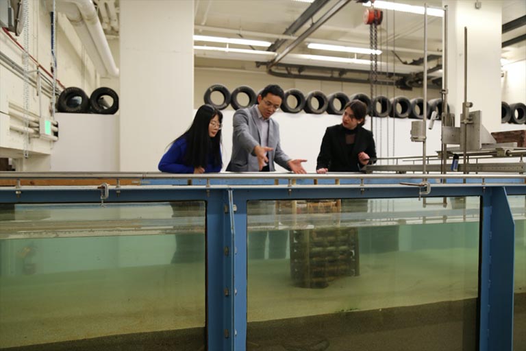 three people stand in front of large tank of water in a lab