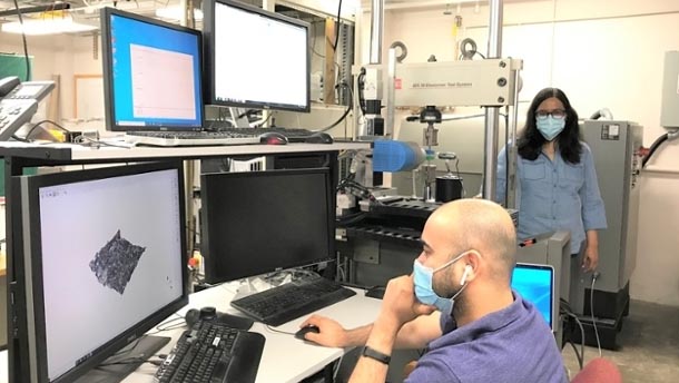 A graduate student and professor, both wearing masks and socially distanced, look at a computer monitor with data.