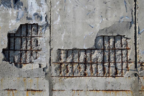 spalling on a concrete wall reveals rusted steel reinforcing embedded within the concrete