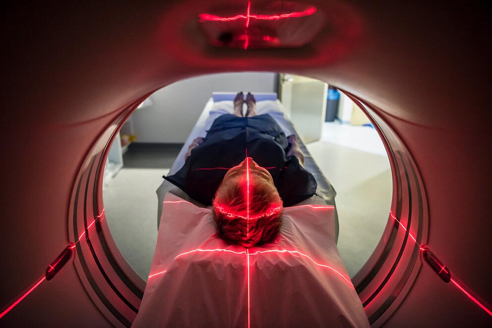 A woman enters an MRI machine with red laser lights covering her head and torso