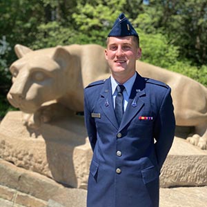 person dressed in air force uniform stands at ease in front of nittany lion statue