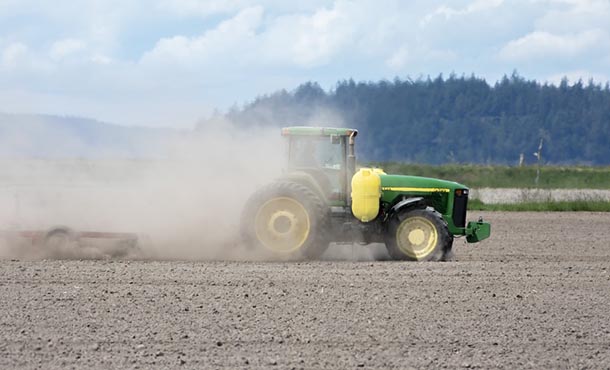 A tractor kicks up a cloud of dust as it moves across a field