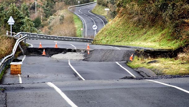 A damaged road shows sections that are cracked and missing