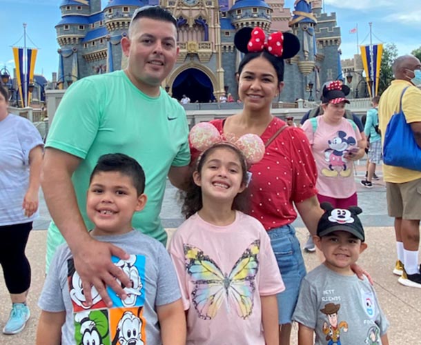 a father, a mother, and their three children pose for a photo in front of castle at Disney World