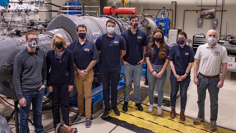 A team of researchers working on sustainable aircraft pose in front of a gas turbine engine.