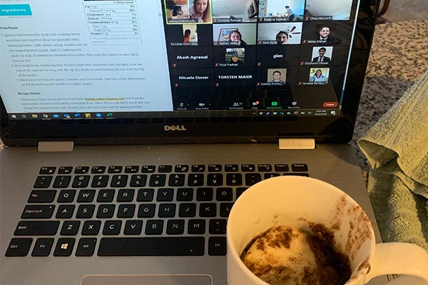 a coffee mug containing cake sits near an open laptop during a Zoom call