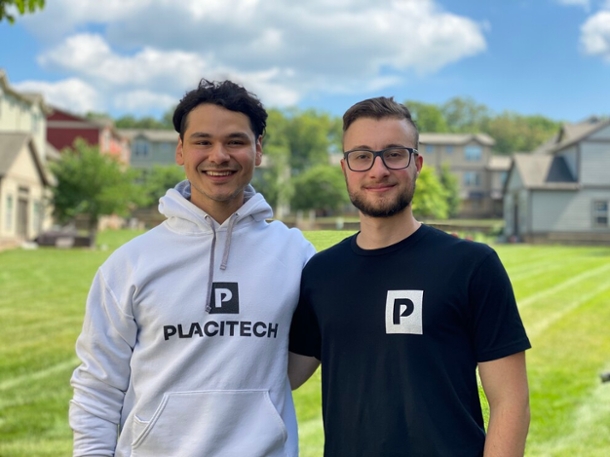 Two smiling male college students wearing a hoodie and a T-shirt pose outdoors. 