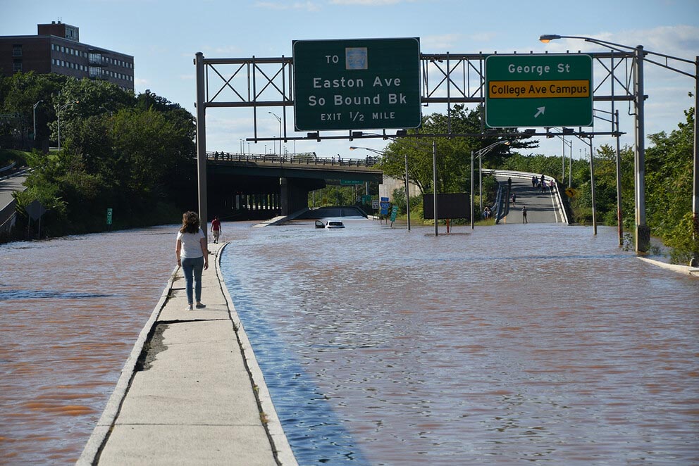 a woman walks on a median strip surrounded by flooded roadways