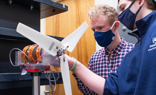 two young men wearing masks adjust a mini-propellor, a portion of a model wind turbine