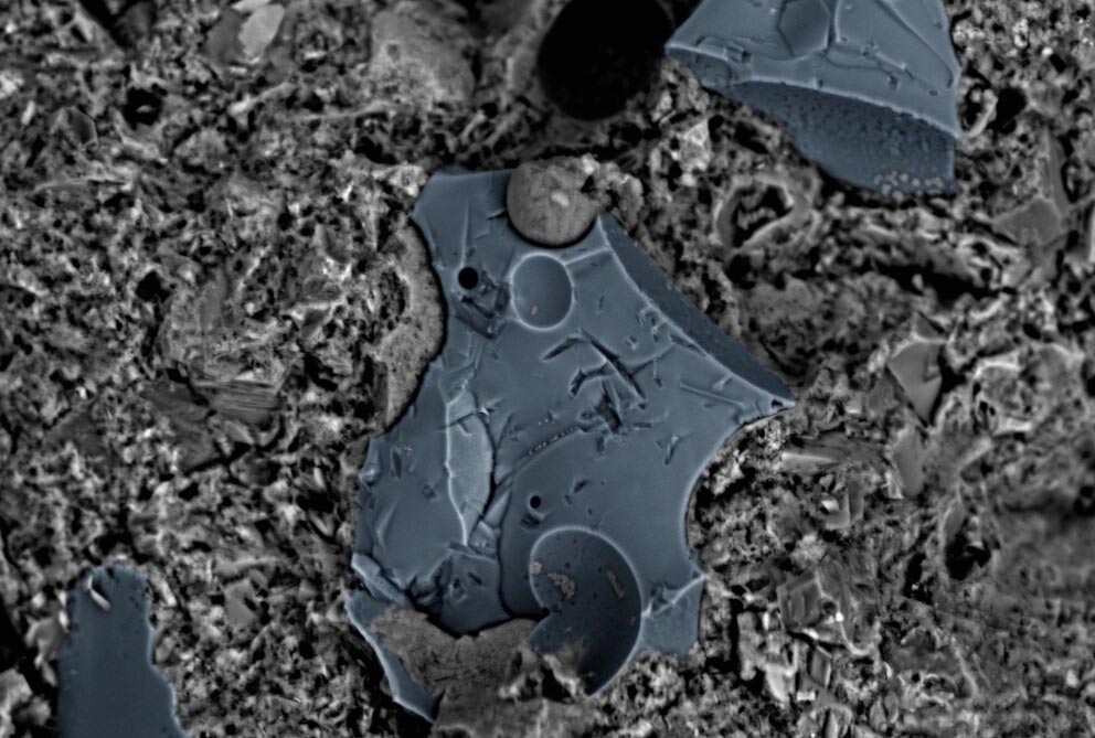 A microscopic image shows irregularly shaped blue-gray plates with concavities mixed with a rough gray material
