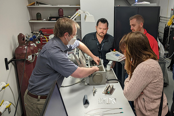 four students in a lab, one demonstrates differential scanning calorimetry on a piece of lab equipment