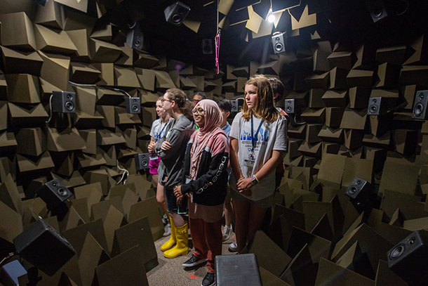 High school students stand in a laboratory with materials and speakers on the walls designed for acoustic testing