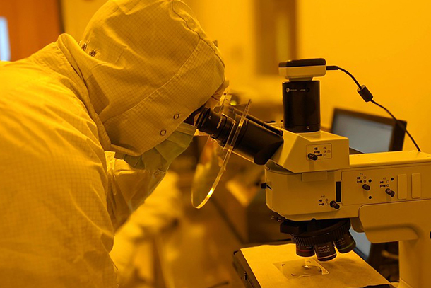 A person in a clean room suit looks through a microscope at semiconductor technology