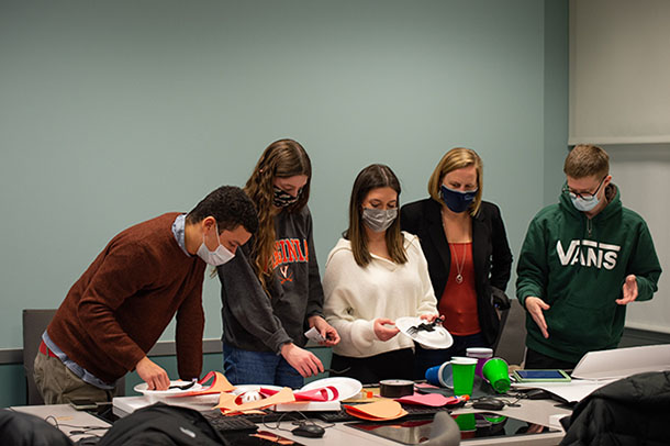 Five people wearing masks stand at a table with paper plates, plastic cups, and construction paper.
