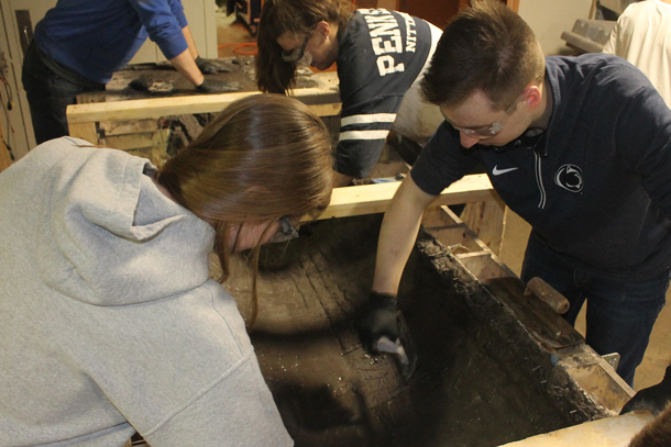 Students using tools to manipulate concrete on the inside of a canoe