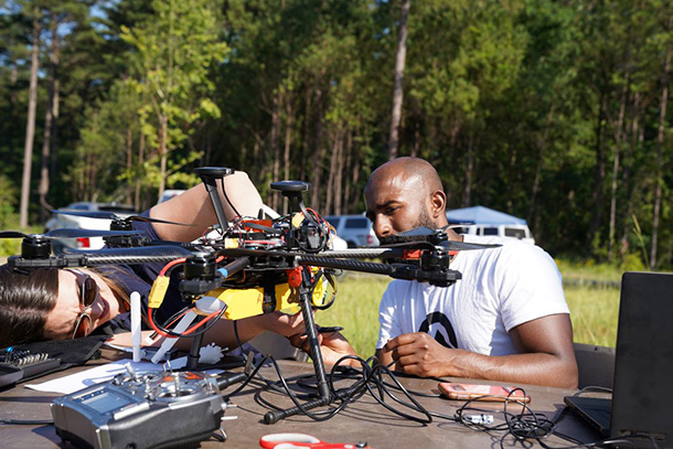 Two individuals adjust a drone on a table