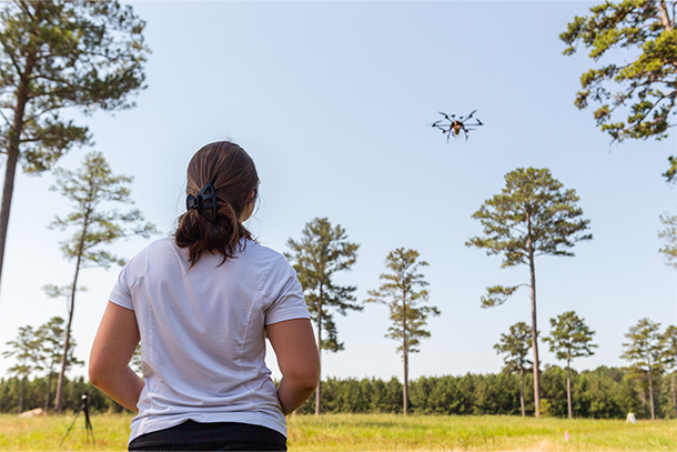 An individual operates a drone in a forested area