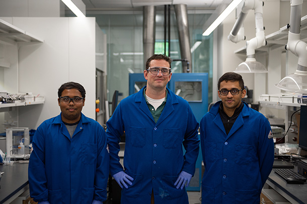 Three individuals wearing lab coats pose in a lab.