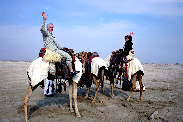 Danner and his wife wave to camera from atop camels in Qatar desert