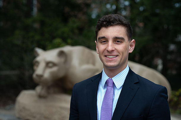 portrait of a man in a suit and tie in front of the Nittany Lion shrine