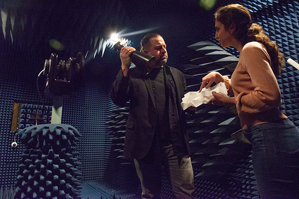 Two researchers stand in an anechoic chamber. One holds a conical horn antenna and one holds an origami frequency selective surface. 